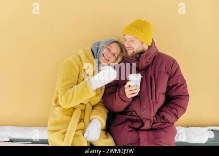 Glückliches Paar, das Kaffee zusammen vor der gelben Wand genießt Stockfoto