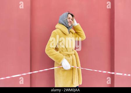 Glückliche junge Frau, die rot-weißes Barrikadenband vor der Pfirsichwand hält Stockfoto