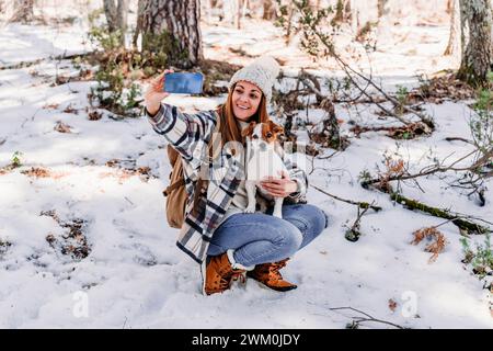 Lächelnder Wanderer, der Selfie mit Hund im Schnee macht Stockfoto