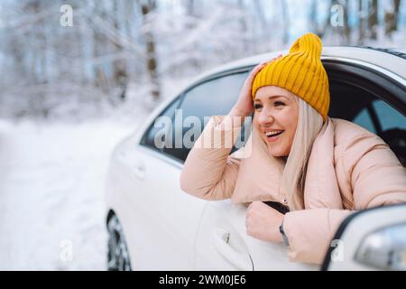 Glückliche Frau mit Kopf in Hand, die sich aus dem Autofenster im Wald beugt Stockfoto