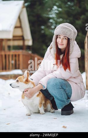 Frau, die warme Kleidung trägt und Corgi im Winter hält Stockfoto