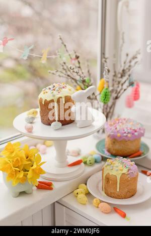 Kuchen mit Blumen und Eiern in der Nähe von Osterhasenspielzeug auf der Fensterbank Stockfoto
