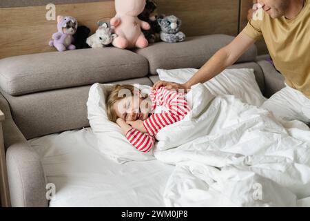 Vater streichelte und weckte eine verspielte Tochter im Bett auf Stockfoto