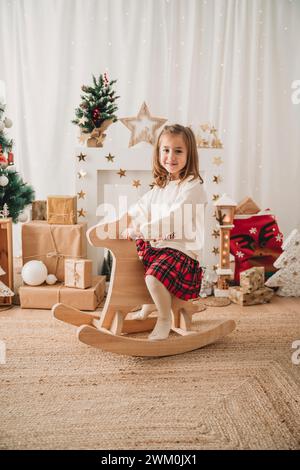 Lächelndes, süßes blondes Mädchen, das zu Hause auf Schaukelpferd sitzt Stockfoto