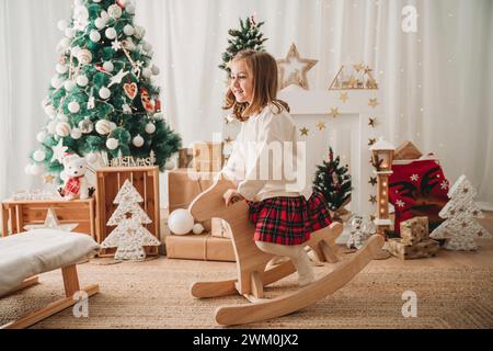 Glückliches Mädchen, das zu Hause auf einem hölzernen Schaukelpferd sitzt Stockfoto