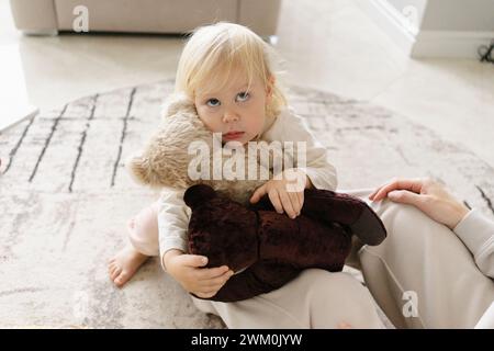 Niedliches Mädchen, das Stoffspielzeug in der Nähe der Mutter zu Hause hält Stockfoto