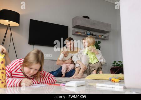 Kinder spielen mit Eltern und Mädchen machen Hausaufgaben zu Hause Stockfoto