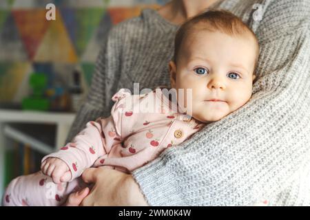 Niedliches Mädchen in den Armen der Mutter zu Hause Stockfoto