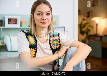 Lächelnde Frau, die Strickjacke trägt und zu Hause sitzt Stockfoto