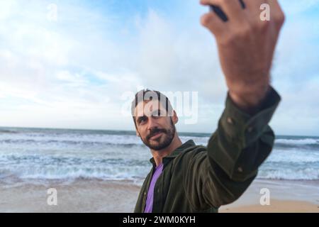 Mann macht Selfie durch Smartphone vor dem Meer am Strand Stockfoto