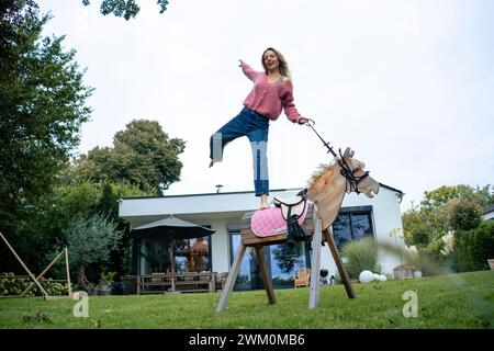 Glückliche Frau, die auf einem Holzpferd steht und in der Nähe des Hauses genießt Stockfoto