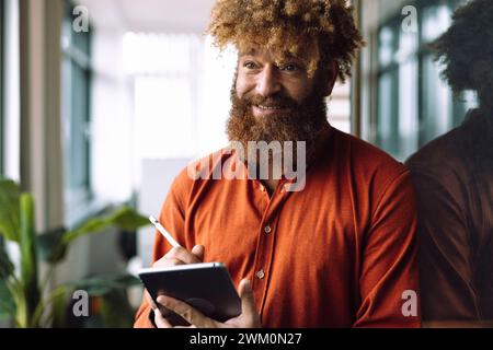 Lächelnder Geschäftsmann, der im Büro einen Tablet-PC mit digitalisiertem Stift hält Stockfoto