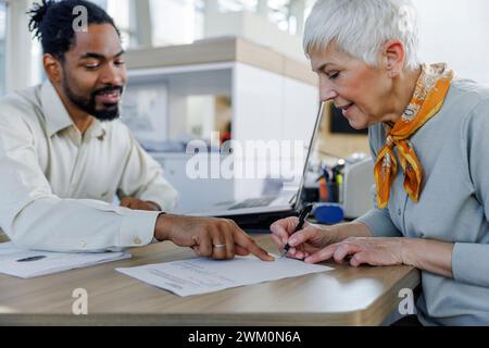 Vertriebsmitarbeiter erklärt dem Kunden, wie er am Schreibtisch Papierkram erledigt Stockfoto