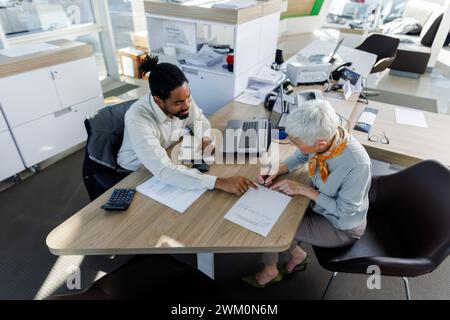 Frau, die einen Vertrag mit einem Verkäufer unterzeichnet, der am Schreibtisch sitzt Stockfoto