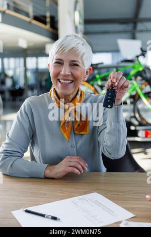 Glückliche Seniorin, die Autoschlüssel am Schreibtisch hält Stockfoto