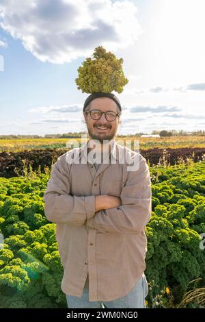 Lächelnder Bauer, der Romanesco Blumenkohl auf dem Kopf auf der Farm ausbalanciert Stockfoto