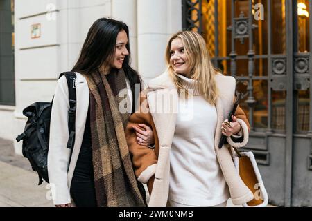 Lächelnde Freunde, die Arm in Arm in der Nähe des Gebäudes laufen Stockfoto