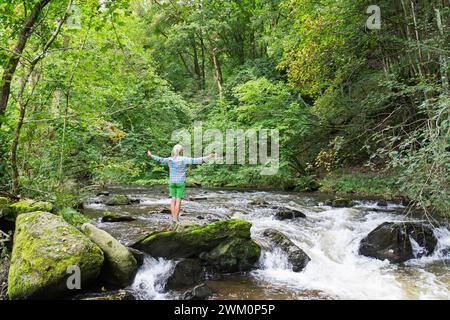 Ältere Frau, die im Wald badete, mit den Armen, die vom Fluss gestreckt wurden Stockfoto