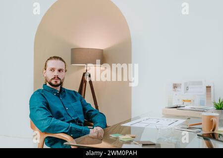Seriöser Innenarchitekt sitzt im Büro auf einem Stuhl Stockfoto
