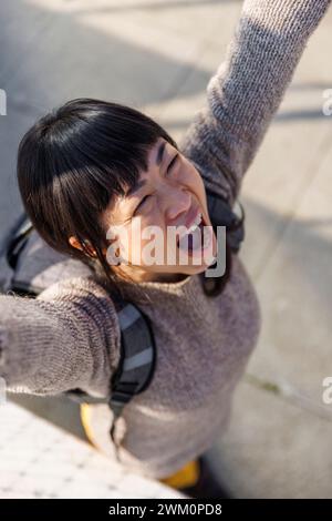 Fröhliche Frau, die mit erhobenen Armen auf dem Fußweg steht Stockfoto