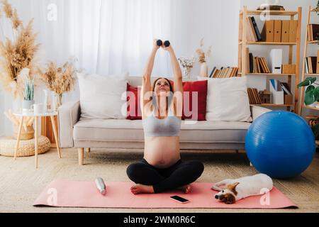 Schwangere Frau, die zu Hause mit Hanteln auf Yogamatte sitzt Stockfoto
