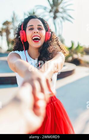 Glückliche Frau, die Musik hört und im Skatepark die Hand eines Freundes hält Stockfoto