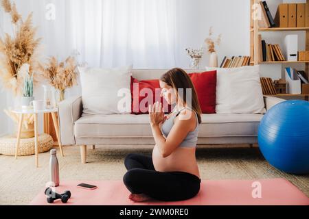 Schwangere Frau, die zu Hause Yoga auf einer Trainingsmatte übt Stockfoto