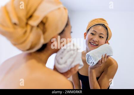 Lächelnde junge Frau, die das Gesicht mit einem Handtuch im Badezimmer zu Hause abwischt Stockfoto