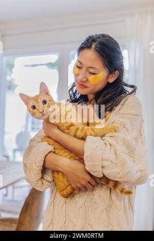 Lächelnde Frau mit Flecken unter den Augen, die Katze zu Hause hält Stockfoto