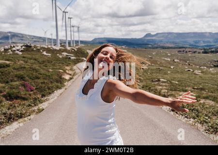 Spanien, Madrid, Porträt einer schwangeren Frau, die mit erhobenen Armen mitten auf der Straße steht und sich an Windparks vorbeizieht Stockfoto