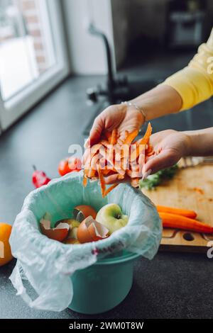 Eine junge Frau, die zu Hause Karottenschalen in den Mülleimer legt Stockfoto