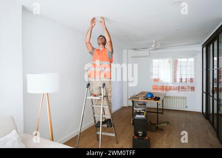 Der Servicemitarbeiter steht auf einer Leiter und arbeitet zu Hause Stockfoto