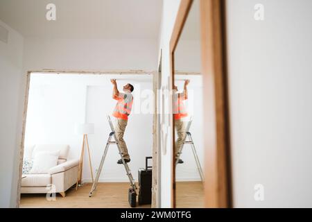 Der Reparaturmann steht auf einer Leiter und untersucht die Decke zu Hause Stockfoto