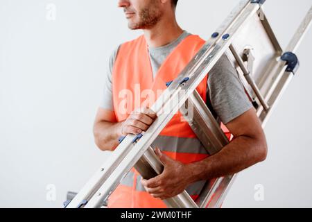 Reifer Techniker, der zu Hause eine Leiter vor der Wand trägt Stockfoto