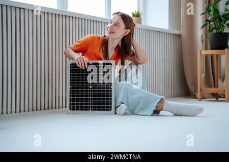 Lächelnde Frau, die zu Hause mit Sonnenkollektor auf dem Boden sitzt Stockfoto