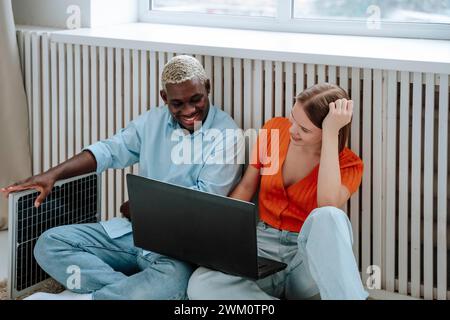 Lächelnde Freiberufler sitzen mit Laptop und Solarpanel in der Nähe des Fensters zu Hause Stockfoto