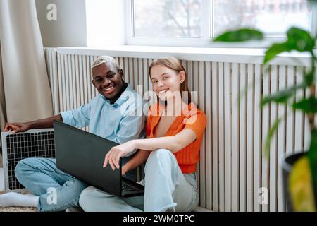 Glücklicher Mann und Frau sitzen mit Laptop in der Nähe des Fensters zu Hause Stockfoto