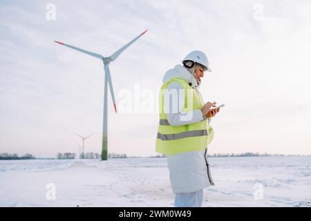 Wartungstechniker mit Smartphone vor der Windturbine Stockfoto