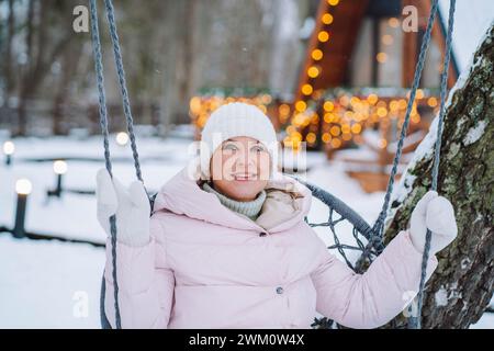 Lächelnde reife Frau, die im Winter auf Schaukel sitzt Stockfoto