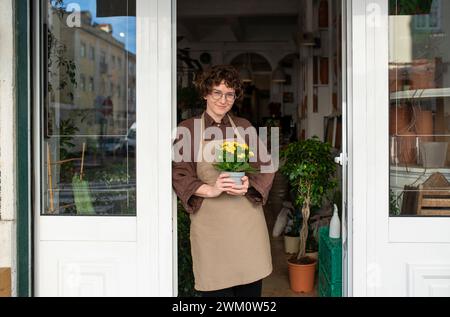 Lächelnder Botaniker, der die Pflanze hält und sich an die Tür des Kindergartens lehnt Stockfoto