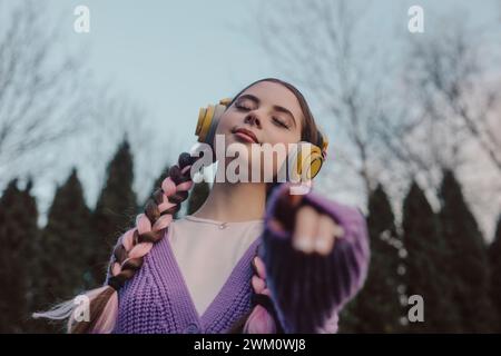 Lächelnde junge Frau mit geschlossenen Augen, die Musik bei Sonnenuntergang hört Stockfoto