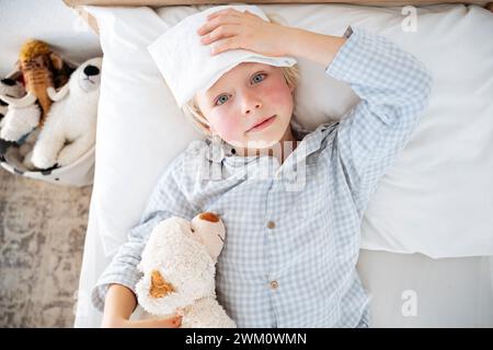 Der kranke Junge liegt zu Hause mit Kompresse über der Stirn auf dem Bett Stockfoto