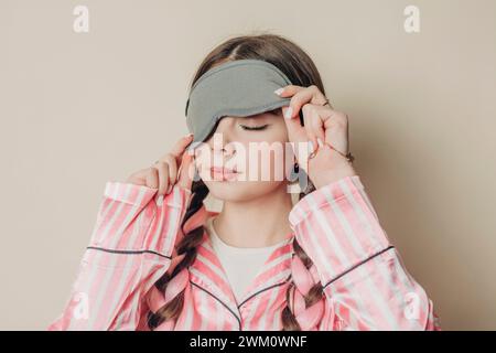 Frau mit Augenmaske und Pyjama vor der Wand Stockfoto