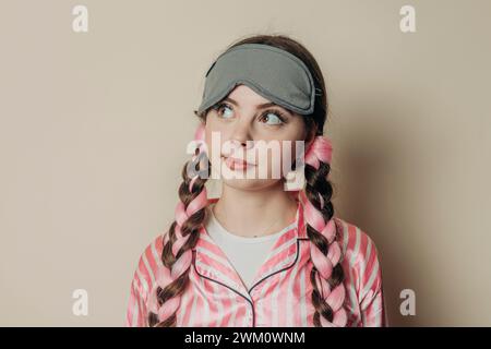 Nachdenkliche Frau mit Augenmaske und Pyjama vor der Wand Stockfoto