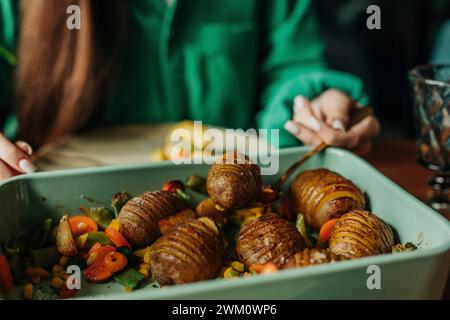 Frau, die beim Osteressen frisch gebackene Kartoffeln aus Auflaufform holt Stockfoto