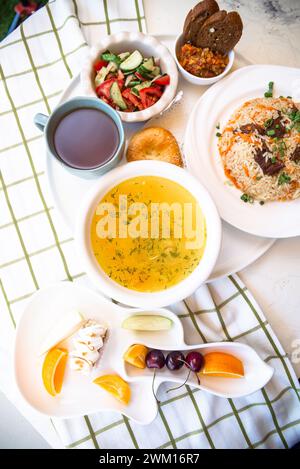 Usbekische Nationalgerichte, Plov, Shurpa, Salat und nicht auf einem Tablett mit Tee. Traditionelle usbekische Küche. Hintergrund mit kariertem Tischtuch. Stockfoto