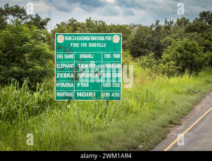 Ein Schild am Straßenrand der Autobahn A7 durch den Mikumi-Nationalpark in Tansania, auf dem Bußgelder für die Straßenabtötung bestimmter Wildtiere vermerkt sind. Stockfoto