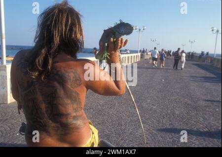 4066275 Lido di Ostia, Italien; (add.info.: Ostia Lido, 1999. Tätowierter Mann mit Leguan. Ostia ist eine Strandstadt in der Nähe von Rom. In der Sommerzeit gehen viele Menschen aus Rom dorthin, besonders junge Vorstädte, die im Slang „coatti“ / Lido di Ostia, 1999, sagten. Uomo tatuato con iguana. Ostia è la spiaggia dei romani. D'Estate è frequentata in cipolare dai giovani che abitano le borgate della periferia, i cosiddetti 'coatti'-); © Marcello Mencarini. Alle Rechte vorbehalten 2024. Stockfoto