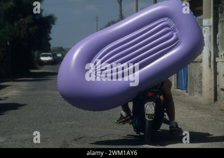 4066285 Lido di Ostia, Italien; (add.info.: Strand Ostia, 1999. Schlauchboot auf einem Motorrad. Ostia ist eine Strandstadt in der Nähe von Rom. In der Sommerzeit gehen viele Menschen aus Rom dorthin, besonders junge Vorstädte, die im Slang „coatti“ / Lido di Ostia, 1999, sagten. Canotto su un motorino. Ostia è la spiaggia dei romani. D'Estate è frequentata in cipolare dai giovani che abitano le borgate della periferia, i cosiddetti 'coatti'-); © Marcello Mencarini. Alle Rechte vorbehalten 2024. Stockfoto