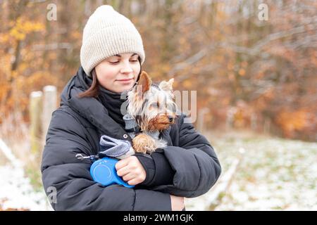 Eine junge Frau, die einen yorkshire-Terrierhund im Winterpark hält. Stockfoto
